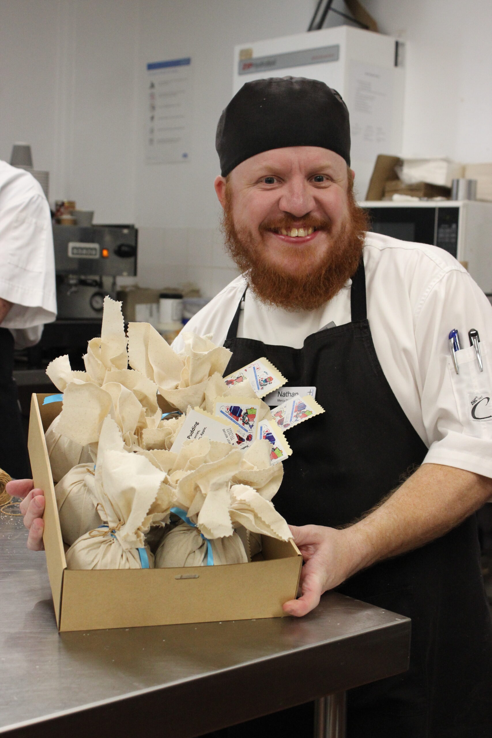 Nathan, one of our Cookery Nook team members smiles at the camera while showing off a box of our Christmas puddings.